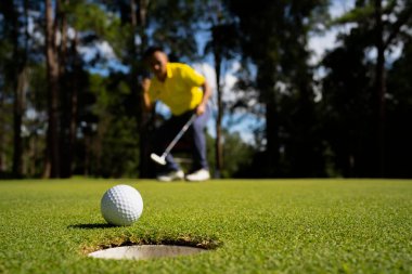 Golfçü topu yeşil golfün üstüne koyuyor, mercek akşam vakti parlıyor. Golf topları gün batımında golf sahasında golf oyuncuları tarafından delik deşik edilecek..