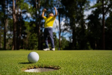 Golfçü topu yeşil golfün üstüne koyuyor, mercek akşam vakti parlıyor. Golf topları gün batımında golf sahasında golf oyuncuları tarafından delik deşik edilecek..