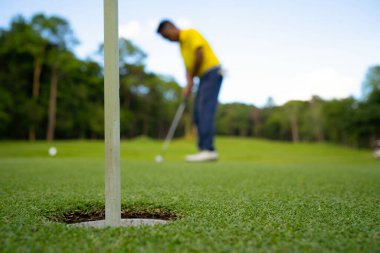 Golfçü topu yeşil golfün üstüne koyuyor, mercek akşam vakti parlıyor. Bulanık golfçü akşam golf sahasında güneş ışığıyla golf oynuyor.. 