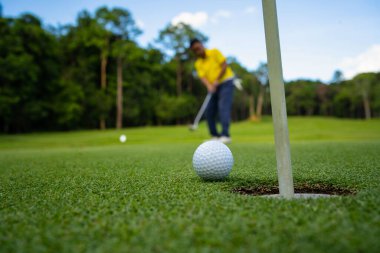 Golfçü topu yeşil golfün üstüne koyuyor, mercek akşam vakti parlıyor. Bulanık golfçü akşam golf sahasında güneş ışığıyla golf oynuyor.. 