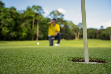 Golfçü topu yeşil golfün üstüne koyuyor, mercek akşam vakti parlıyor. Bulanık golfçü akşam golf sahasında güneş ışığıyla golf oynuyor.. 