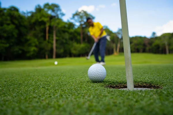 Golfçü topu yeşil golfün üstüne koyuyor, mercek akşam vakti parlıyor. Bulanık golfçü akşam golf sahasında güneş ışığıyla golf oynuyor.. 
