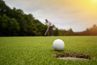 Golfçü topu yeşil golfün üstüne koyuyor, mercek akşam vakti parlıyor. Bulanık golfçü akşam golf sahasında güneş ışığıyla golf oynuyor.. 