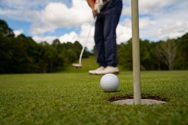 Golfçü topu yeşil golfün üstüne koyuyor, mercek akşam vakti parlıyor. Bulanık golfçü akşam golf sahasında güneş ışığıyla golf oynuyor.. 