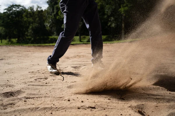 Asian golfer swings in a sand pit during pre-match practice at a golf course. A professional golfer hitting his ball out of a bunker with the sand and ball in mid-air.