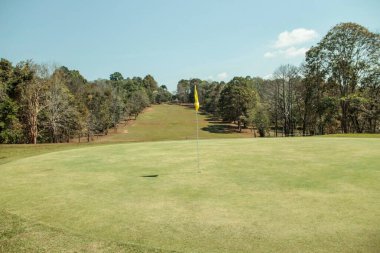 Kırsal kesimde gün batımında güzel bir golf sahasının manzarası. Güneş doğarken golf sahasında sarı bayrak.       