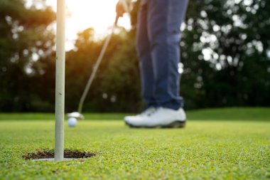 Golfçü topu yeşil golfün üstüne koyuyor, mercek akşam vakti parlıyor. Bulanık golfçü akşam golf sahasında güneş ışığıyla golf oynuyor.. 
