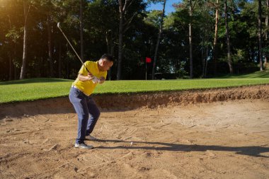 Asyalı golfçü bir golf sahasında maç öncesi antrenman sırasında kum havuzunda sallanıyor. Profesyonel bir golfçü topunu kumla sığınaktan dışarı atıyor.. 