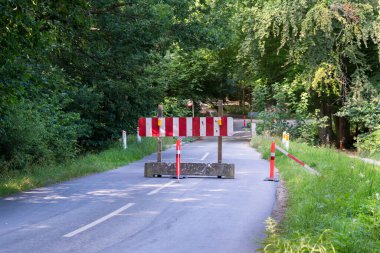 Narrow forest road closed with red and white sign on a concrete block