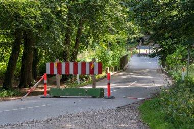 Narrow forest road closed for repairs with red and white sign on a concrete block