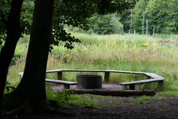 Benches in a circle around a fireplace in the forest next to a lake