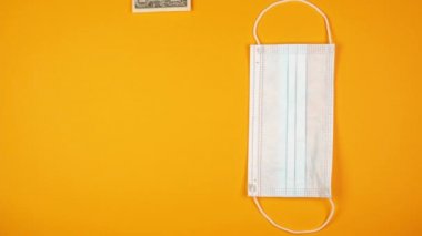 Mavi lastik eldivenli bir erkek, dolar koyar ve parlak sarı arka planda anti-virüs kullan-at yüz maskesi alır.