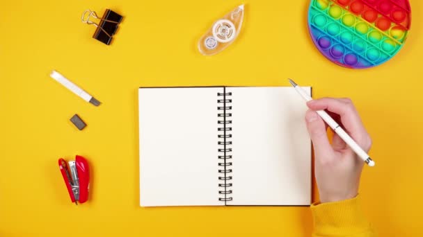 女手抛掷彩虹彩抗压玩具 用记事本 钢笔和其他文具在明亮的黄色背景上弹奏 — 图库视频影像