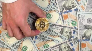 Genç bir erkeğin eli ya da tüccarın eli, arka planda 100 dolarlık banknotların üzerine metalik altın bir bitcoin koyar.