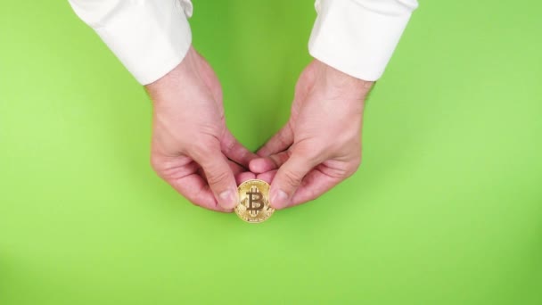 若い成功した投資家やトレーダーの手は 緑の背景に黄金のビットコインを保持します — ストック動画