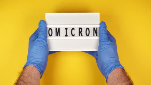 一位戴蓝色橡胶防护手套的年轻男医生的手拿着一个标有Omicron字样的标志 — 图库视频影像