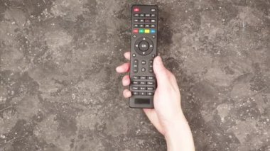 Gri arka planda akıllı televizyon kumandası tutan genç bir kadın.