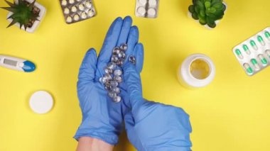 Mavi koruyucu eldivenli bir doktorun ellerinde sarı bir zemin üzerinde D vitamini hapları ve bir sürü ilacın kabarcıkları var.