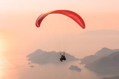 Gökyüzünde yamaç paraşütü olan gün batımı manzarası. Günbatımında Akdeniz üzerinde uçan paraglider ikilisi.