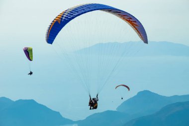 Gökyüzünde paraşütle atlıyor. Paraglider gün batımında dağlarla birlikte denizin üzerinde uçuyor. Oludeniz, Mugla, Türkiye 'de paraglider ve Mavi Göl' ün hava manzarası.