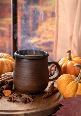 Renkli bir sonbahar arka planına sahip pencerenin yanında dumanı tüten sıcak çikolata ve mini balkabakları.