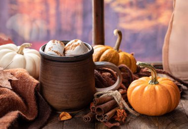 Bir bardak sıcak çikolata, marşmelov ve balkabağı, sonbahar arkaplanı olan bir pencerenin yanındaki ahşap masada.