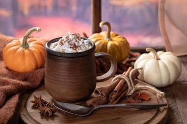 Balkabağı aromalı latte, ahşap bir tabakta tarçın çubukları ve sonbahar arkaplanı olan pencerenin yanında mini balkabakları.