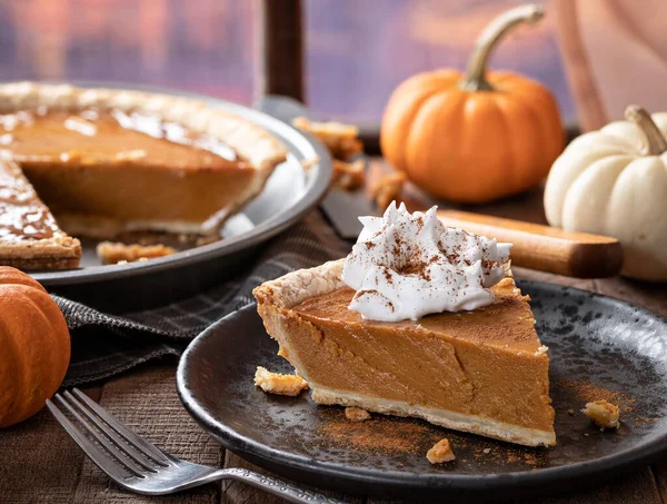 Slice of pumpkin pie with whipped cream and cinnamon with pumpkins in background by a window