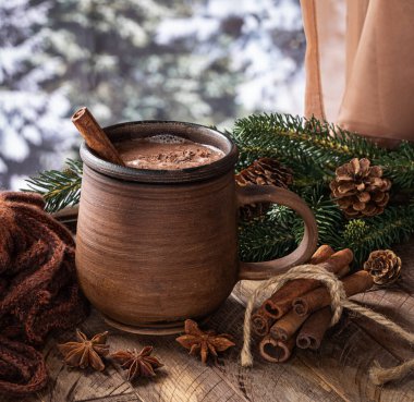 Bir bardak sıcak çikolata ve ahşap bir masa üzerinde tarçın. Arka planda kış mevsimi olan pencerenin yanında.