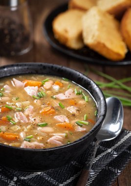 Bir kase jambon ve fasulye çorbası. Köy ahşap bir masada havuç ve soğan.