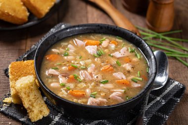 Bir kase jambon ve fasulye çorbası. Köy ahşap bir masada havuç ve soğan.