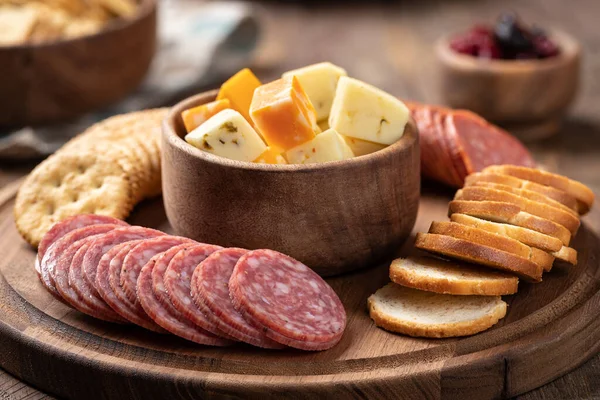 Dilimlenmiş salam, kraker, kızarmış mermiler ve kase içinde peynir küpleriyle atıştırma tabağı.