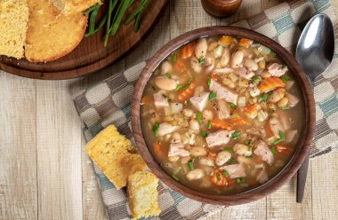 Köy ahşap bir masada mısır ekmeği ile bir kâse içinde jambon ve fasulye çorbası.