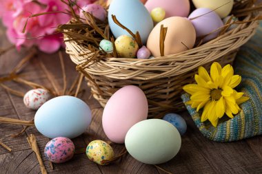 Pastel renkli Paskalya yumurtaları ve sepetteki şekerler ve renkli çiçeklerle dolu ahşap bir masa üzerinde.