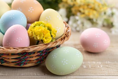 Sarı çiçekli sepetteki renkli paskalya yumurtalarının ve kırsal ahşap bir masanın üzerinde.