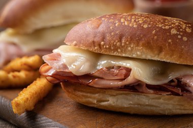 Sıcak jambonlu ve peynirli sandviç ve tahta kesme tahtasının üstünde patates kızartması.