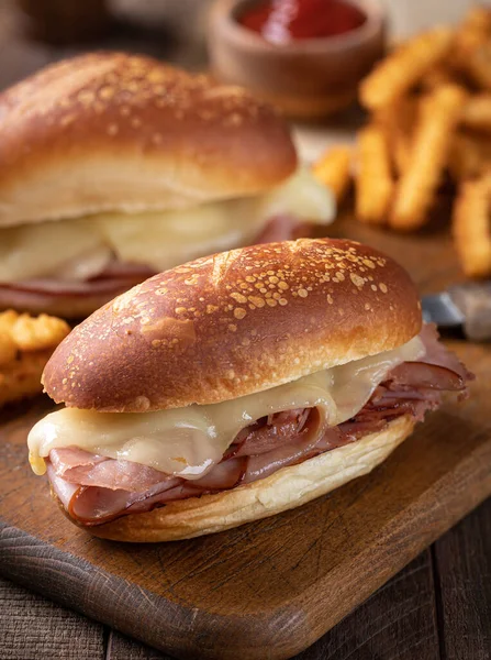 Tahta kesme tahtasının üzerinde patates kızartması ve jambonlu peynirli sandviç.