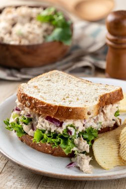 Tabakta patates cipsi ve tahıllı ekmeğin üstünde ton balığı salatası ve marullu sandviç.