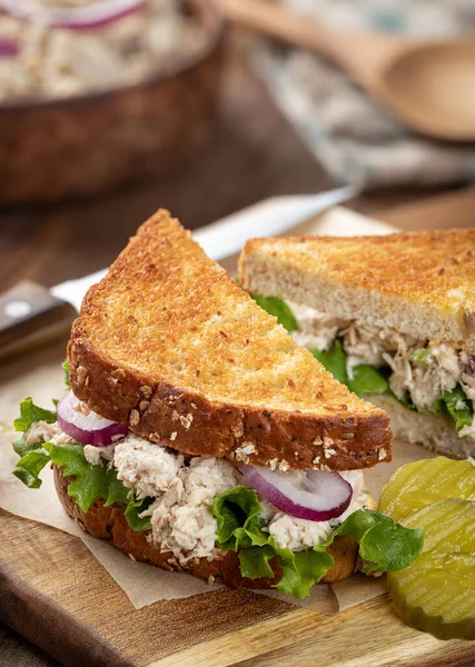 Tuna salad sandwich with lettuce and onion on whole grain bread cut in half on a cutting board