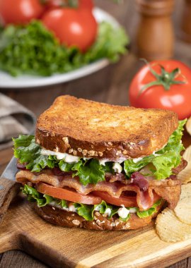 Domuz pastırması, marul ve domatesli sandviç. Tahta kesme tahtasının üstünde tam tahıllı ekmek.