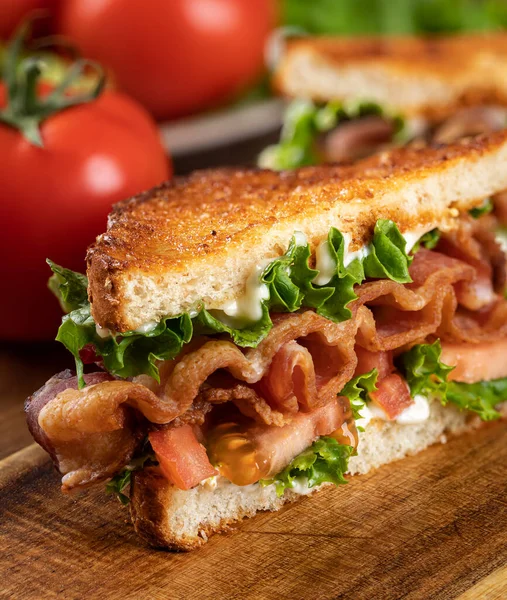 Domuz pastırması, marul ve domatesli sandviçin kapanışı. Tahta kesme tahtasıyla ikiye bölünmüş kepekli tam tahıllı ekmek.