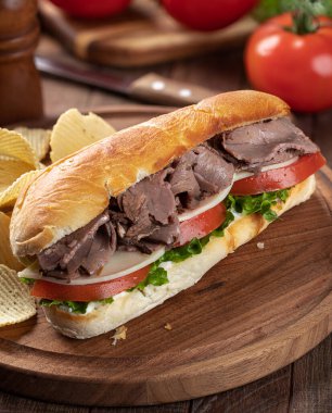 Kızarmış biftekli, peynirli, domatesli ve salatalı sandviç ve patates cipsi.