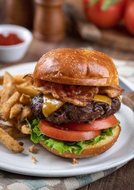 Kızarmış ekmeğin üstünde marul ve domatesli pastırmalı çizburger ve tabakta patates kızartması.