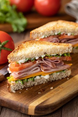 Peynirli jambonlu sandviç, marul ve domatesli tam tahıllı ekmek. Arka planda marul ve domates