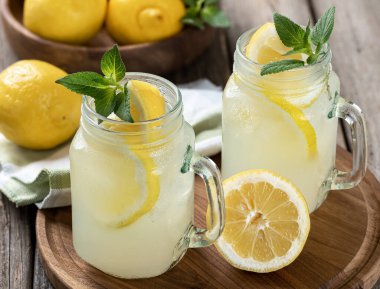 Arka planda bir kase limon ve ahşap tepside naneli iki bardak limonata.