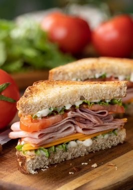 Peynirli jambonlu sandviç, marul ve domatesli tam tahıllı ekmek. Arka planda marul ve domates