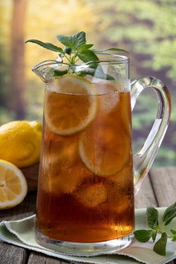 Bir sürahi buzlu çay, buz, limon ve naneli eski ahşap masa ve kırsal arka plan