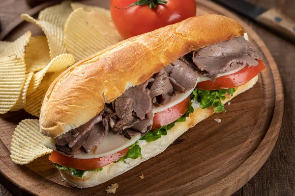 Kızarmış biftekli, peynirli, domatesli ve salatalı sandviç ve patates cipsi.