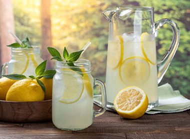 Limonata, limon dilimleri ve bardakta naneli sürahi ve arka planda limonlu tahta masa ve kırsal arka plan.