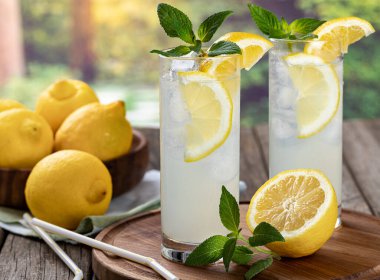 İki bardak limon dilimli soğuk limonata, kırsal bir zeminde nane ve buz küpleri.